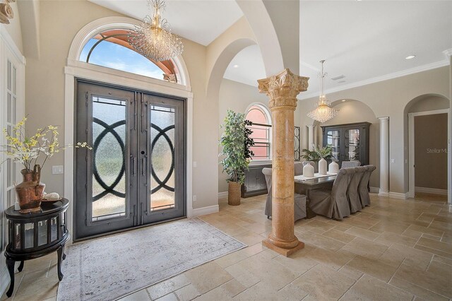 tiled entrance foyer featuring a chandelier, crown molding, french doors, and ornate columns