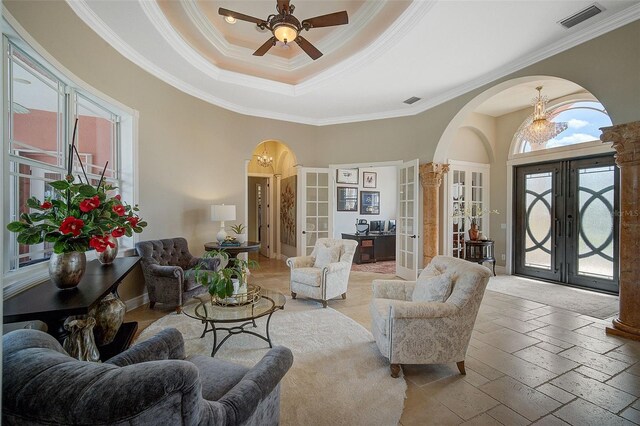 tiled living room with ceiling fan with notable chandelier, a tray ceiling, french doors, and ornamental molding