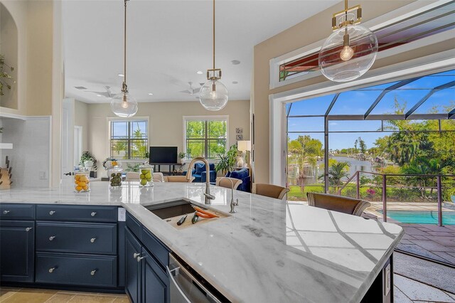 kitchen featuring pendant lighting, light stone countertops, ceiling fan, backsplash, and sink