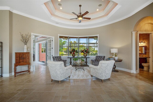 tiled living room with a raised ceiling, ceiling fan, decorative columns, and ornamental molding