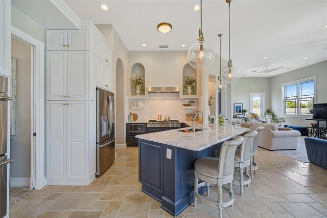 kitchen with sink, a kitchen breakfast bar, light stone countertops, stainless steel refrigerator with ice dispenser, and white cabinetry