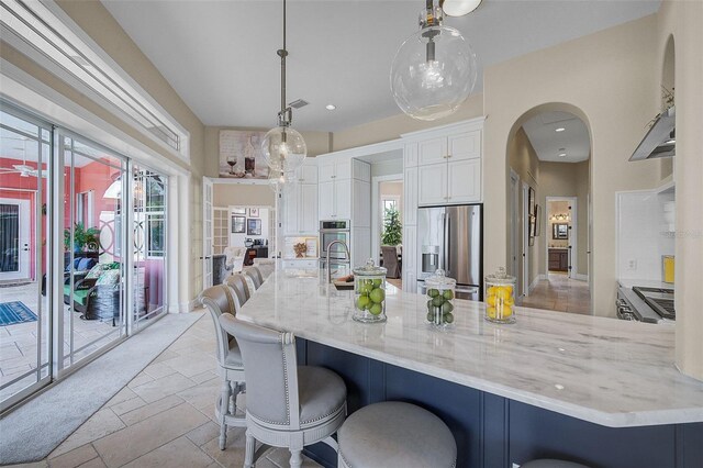 kitchen with stainless steel fridge with ice dispenser, white cabinets, a breakfast bar, light stone countertops, and decorative light fixtures