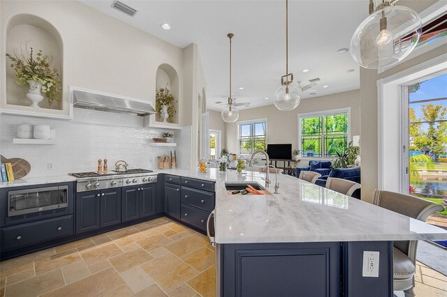 kitchen featuring stainless steel appliances, light tile floors, light stone counters, wall chimney range hood, and tasteful backsplash