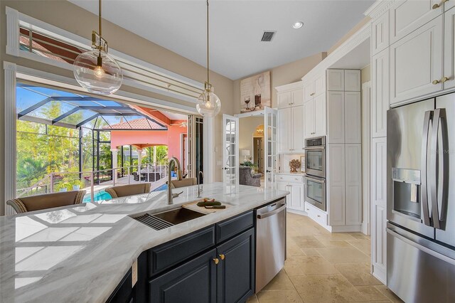 kitchen featuring stainless steel appliances, decorative light fixtures, sink, white cabinets, and light stone counters