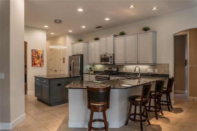 kitchen featuring appliances with stainless steel finishes, a kitchen bar, sink, dark stone countertops, and light tile patterned flooring