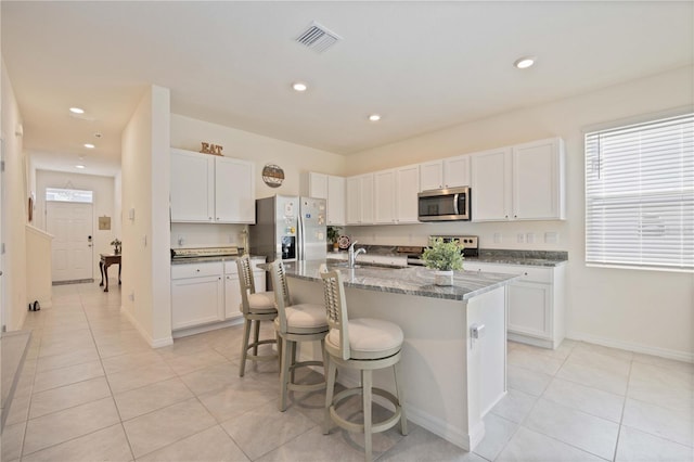 kitchen featuring an island with sink, light stone counters, appliances with stainless steel finishes, and white cabinetry