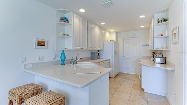 kitchen with kitchen peninsula, light tile floors, white cabinetry, and sink