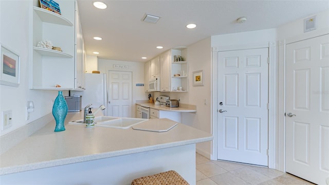 kitchen with kitchen peninsula, white appliances, sink, light tile floors, and white cabinets