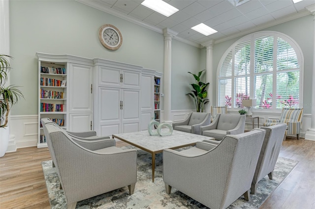 living room with crown molding, a high ceiling, light wood-type flooring, and ornate columns