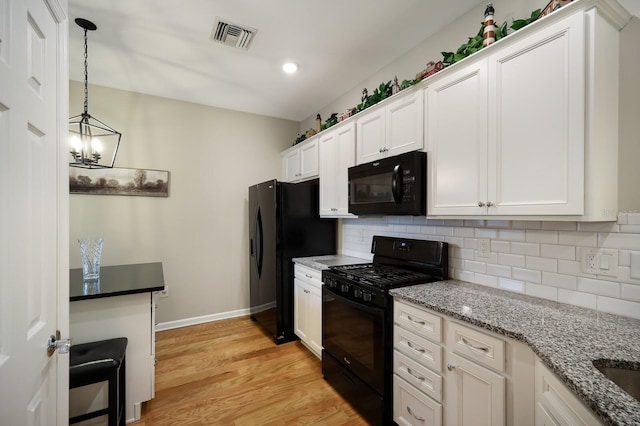 kitchen featuring light stone countertops, white cabinetry, hanging light fixtures, and black appliances