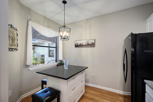 kitchen with black fridge, light hardwood / wood-style floors, decorative light fixtures, a breakfast bar, and white cabinets