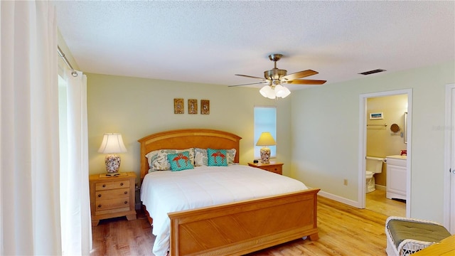 bedroom with a textured ceiling, ensuite bathroom, light hardwood / wood-style flooring, and ceiling fan