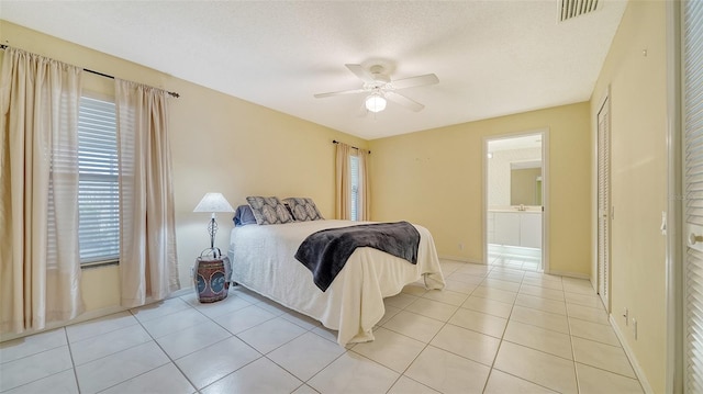 tiled bedroom with ensuite bathroom, multiple windows, ceiling fan, and a textured ceiling