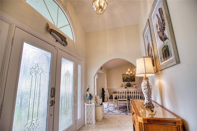 tiled foyer entrance with high vaulted ceiling, french doors, and a notable chandelier