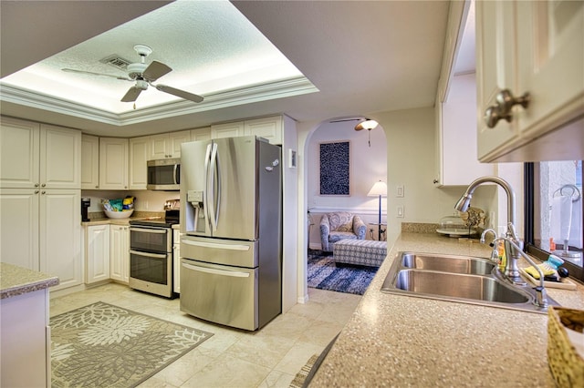 kitchen featuring stainless steel appliances, a tray ceiling, ornamental molding, sink, and ceiling fan