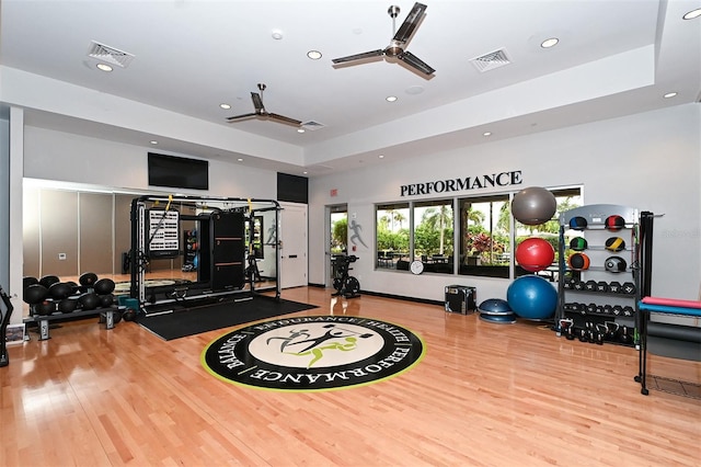 workout area with a raised ceiling, light hardwood / wood-style floors, and ceiling fan