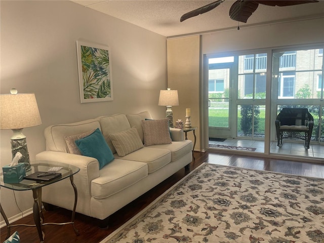 living room featuring ceiling fan, a textured ceiling, and dark wood-type flooring