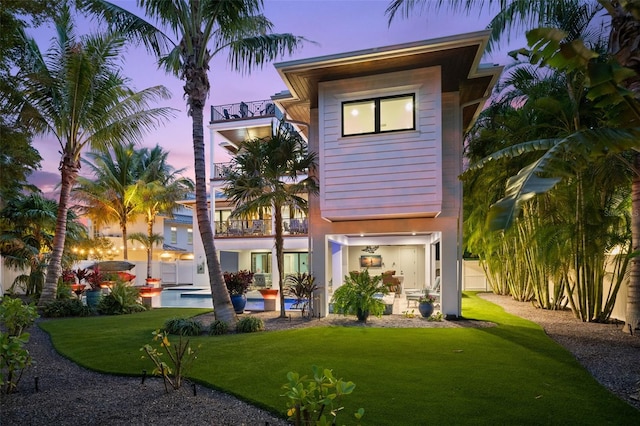 back house at dusk with a yard, a patio, and a balcony