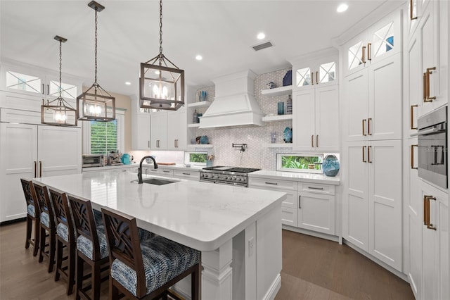 kitchen featuring premium range hood, sink, white cabinets, stainless steel appliances, and a center island with sink