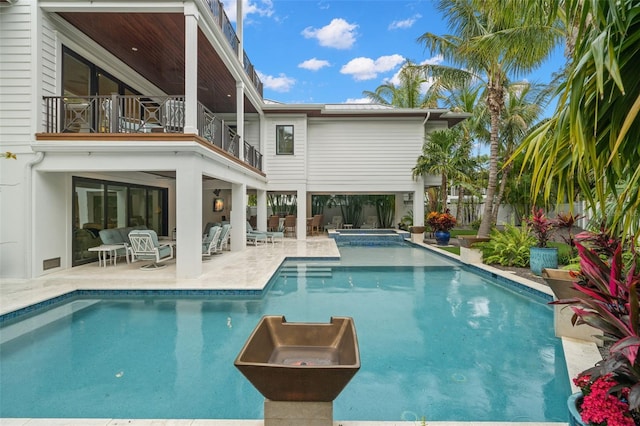 rear view of house with a fenced in pool, a patio, and a balcony