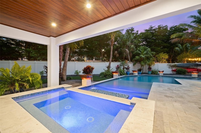 pool at dusk featuring an in ground hot tub, pool water feature, and a patio