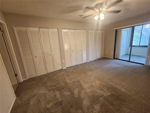 unfurnished bedroom with a textured ceiling, multiple closets, dark colored carpet, and ceiling fan