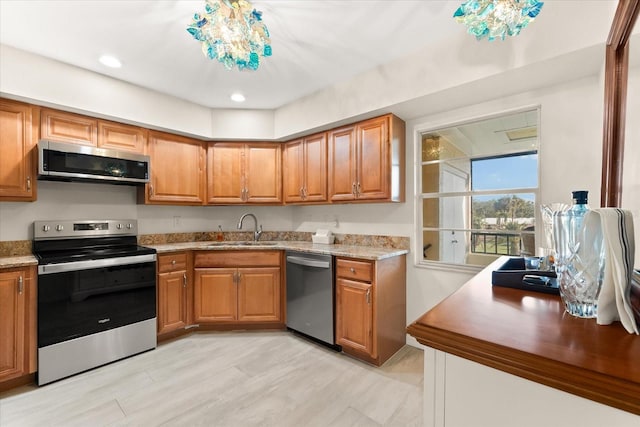 kitchen with a notable chandelier, appliances with stainless steel finishes, light stone counters, and sink