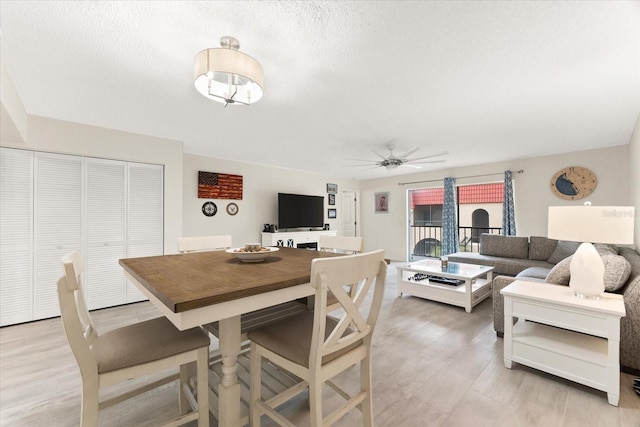 dining area featuring light hardwood / wood-style flooring, a textured ceiling, and ceiling fan with notable chandelier