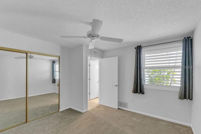 unfurnished bedroom featuring ceiling fan, a closet, light carpet, and a textured ceiling