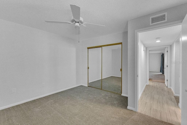 unfurnished bedroom with light carpet, a textured ceiling, a closet, and ceiling fan