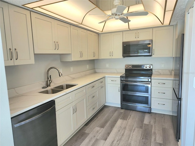 kitchen with light stone countertops, appliances with stainless steel finishes, ceiling fan, sink, and light hardwood / wood-style floors