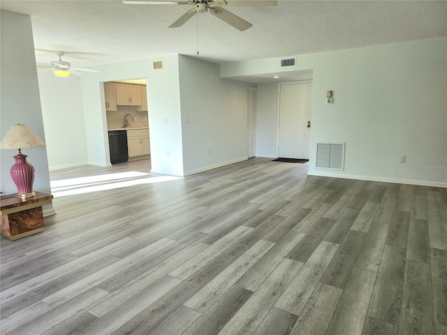 unfurnished living room featuring ceiling fan, sink, a textured ceiling, and light hardwood / wood-style flooring