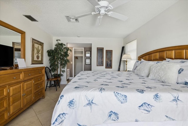 bedroom featuring ceiling fan, a closet, light tile floors, and a textured ceiling