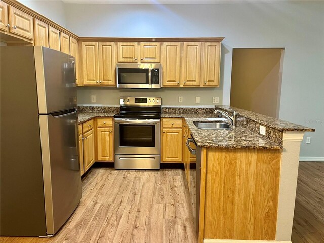 kitchen featuring dark stone counters, sink, appliances with stainless steel finishes, light hardwood / wood-style flooring, and kitchen peninsula