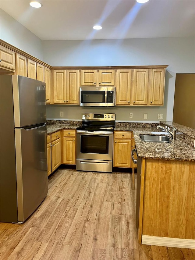 kitchen featuring dark stone counters, stainless steel appliances, sink, light hardwood / wood-style flooring, and kitchen peninsula