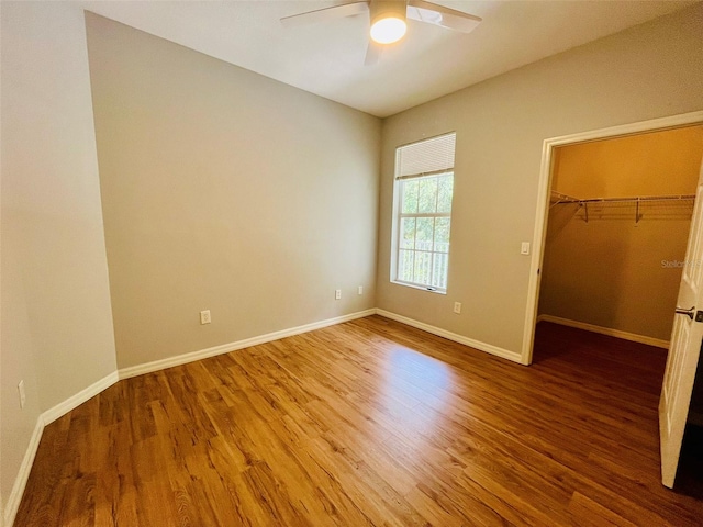 unfurnished bedroom with a closet, hardwood / wood-style flooring, a spacious closet, and ceiling fan