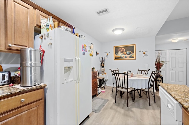 kitchen with white refrigerator with ice dispenser, light stone countertops, and light wood-type flooring