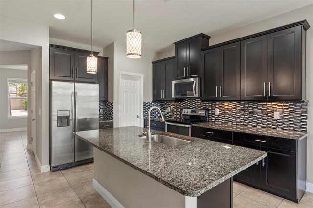 kitchen featuring appliances with stainless steel finishes, sink, an island with sink, hanging light fixtures, and light tile patterned flooring