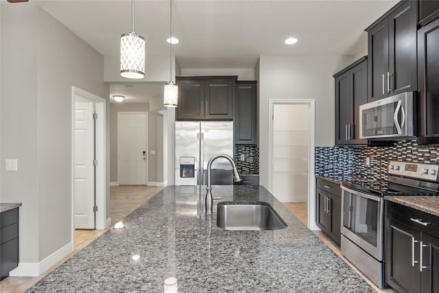 kitchen with sink, hanging light fixtures, stainless steel appliances, tasteful backsplash, and dark stone countertops