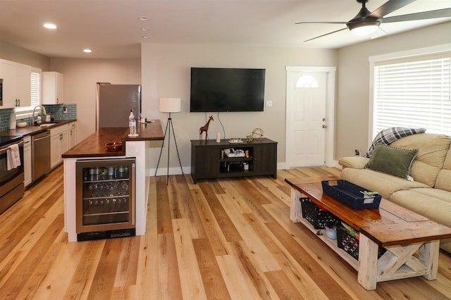 living room featuring light hardwood / wood-style floors, sink, ceiling fan, and wine cooler