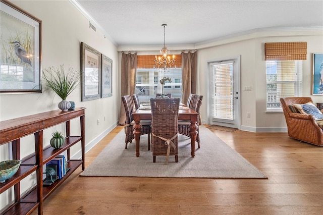 dining space with crown molding, an inviting chandelier, light wood-type flooring, and a wealth of natural light