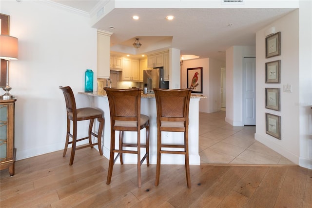 kitchen featuring light stone countertops, high quality fridge, kitchen peninsula, ornamental molding, and a breakfast bar area