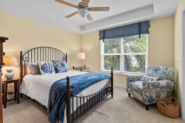 carpeted bedroom with ceiling fan, a tray ceiling, and multiple windows