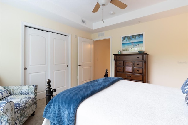 carpeted bedroom featuring a closet, ceiling fan, and a raised ceiling