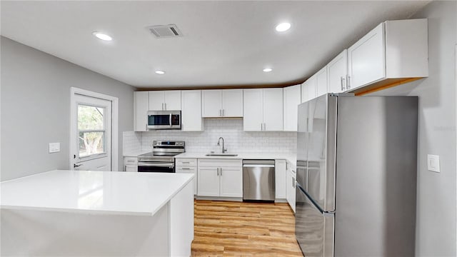 kitchen featuring sink, backsplash, light hardwood / wood-style floors, stainless steel appliances, and white cabinetry