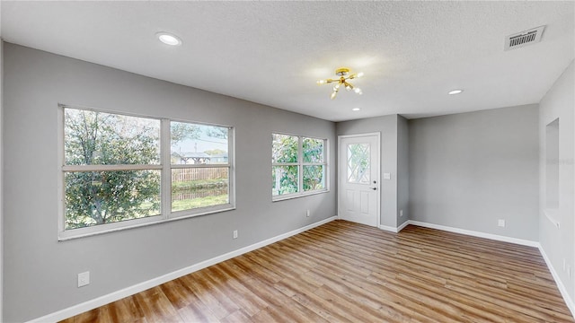 empty room with a textured ceiling, a chandelier, and light wood-type flooring