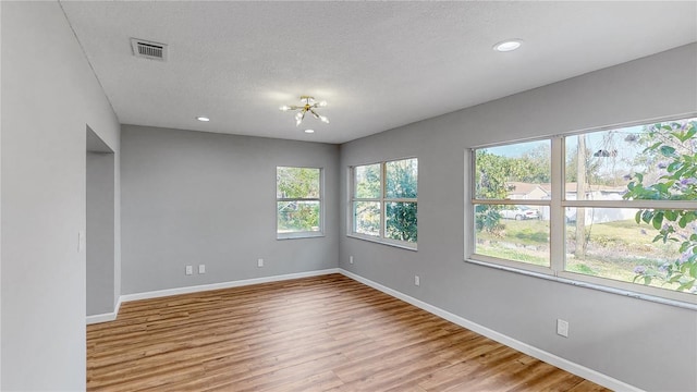 spare room featuring a notable chandelier, a textured ceiling, and light hardwood / wood-style floors