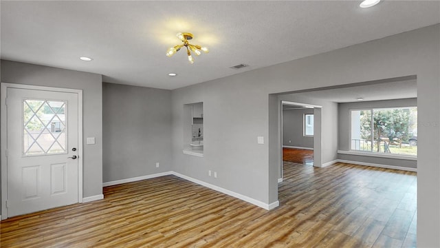 entrance foyer with an inviting chandelier, a textured ceiling, light hardwood / wood-style floors, and a healthy amount of sunlight