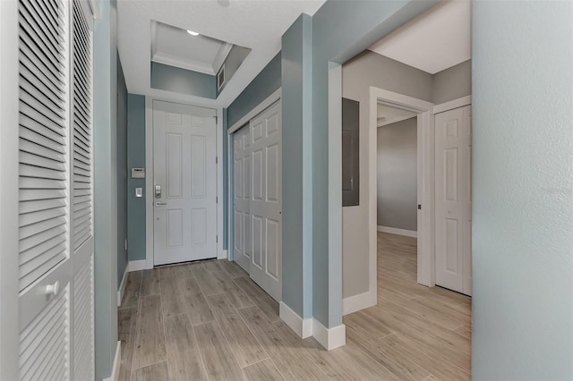 hallway featuring ornamental molding, a raised ceiling, and light hardwood / wood-style flooring