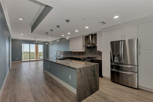 kitchen featuring white cabinetry, hanging light fixtures, appliances with stainless steel finishes, sink, and wall chimney range hood